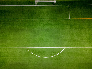 Aerial top-down view of a football field with a green artificial turf, white goalpost, and visible field markings under bright lighting