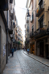 Fototapeta premium Tourists walking down narrow cobblestone street in girona, spain