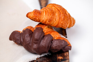 Delicious croissants with chocolate coating served on a wooden board