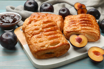 Delicious puff pastries and plums on light blue wooden table, closeup