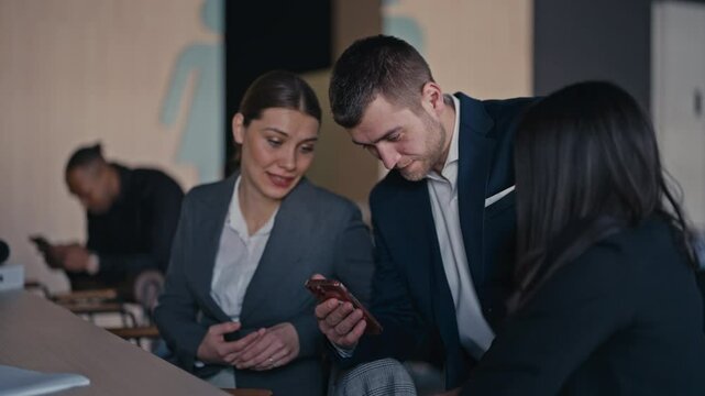 Colleagues in formal business attire enjoying a lighthearted moment during a break, sharing a laugh while looking at content on a smartphone. Concept of workplace relaxation and camaraderie.