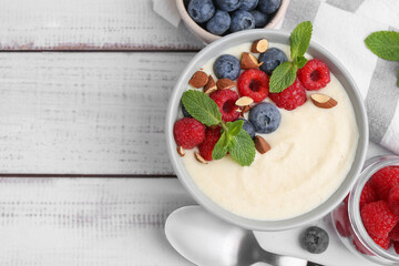 Tasty cooked semolina porridge with almonds, berries and mint on white wooden table, top view. Space for text