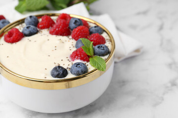 Tasty cooked semolina porridge with berries and mint on white marble table, closeup. Space for text