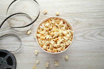 Tasty popcorn and film reel on white wooden background, flat lay