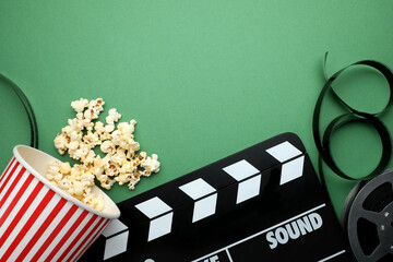 Movie clapper, tasty popcorn and film reel on green background, flat lay. Space for text