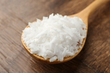 Spoon with white soy wax flakes on wooden table, closeup