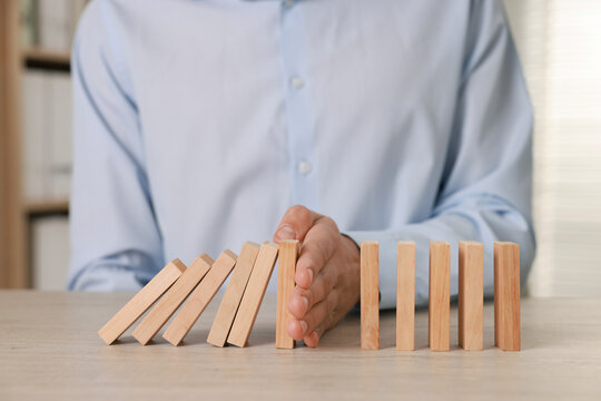 Man stopping wooden blocks from falling at table, closeup. Domino effect