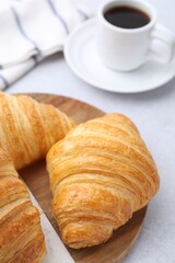 Tasty fresh croissants and cup of coffee on light table, closeup
