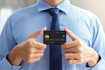 Business man with blue suits and necktie showing mockup black credit card with two hande and blurry background