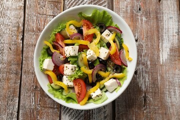 Delicious fresh Greek salad in bowl on wooden table, top view