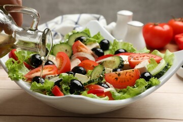 Adding olive oil to Greek salad at white wooden table, closeup