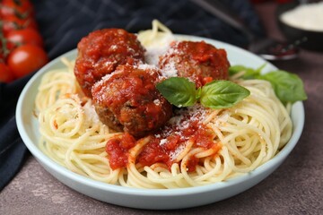 Delicious pasta with meatballs, basil and cheese on brown textured table, closeup