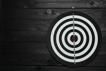 One dart board hanging on black wooden background. Space for text