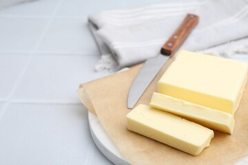 Cut block of fresh butter and knife on white tiled table, closeup. Space for text