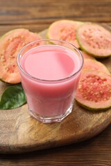 Tasty guava juice in glass, leaf and slices of fruits on wooden table, closeup