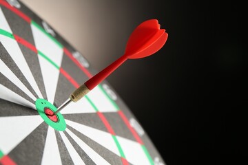 Red arrow hitting target on dart board against black background, closeup