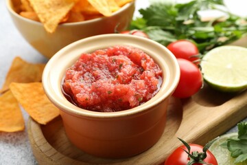 Spicy salsa sauce in bowl, nachos and ingredients on table, closeup