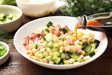 Making okroshka soup. Pouring kvass into bowl with different ingredients on wooden table, closeup