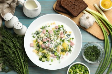 Delicious okroshka soup in bowl and products on light blue wooden table, flat lay