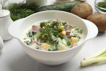 Delicious okroshka soup in bowl and ingredients on white table, closeup