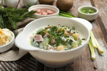 Delicious okroshka soup in bowl and ingredients on wooden table, closeup