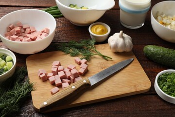 Cut ingredients for okroshka soup and knife on wooden table, closeup