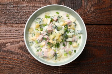 Delicious okroshka soup in bowl on wooden table, top view