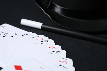 Playing cards, hat and magic wand on black background, closeup