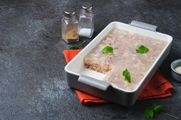 Cold appetizer, meat jelly or aspic  with turkey and pork in a rectangular ceramic form on a dark concrete background.