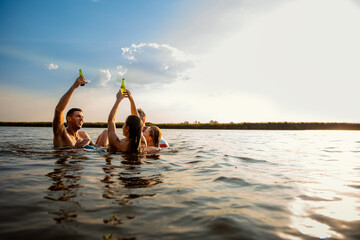 Group of young friends having fun and enjoying a summer day swimming with rubber tube and drinking beer at the lake.