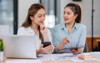 Asian Business women using calculator and laptop for doing math finance on an office desk, tax, report, accounting, statistics, and analytical research concept
