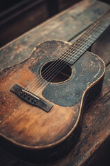 Obraz premium A captivating close-up photograph of a vintage acoustic guitar resting on a rustic wooden table, with soft natural lighting highlighting its intricate wood grain and fretboard details,