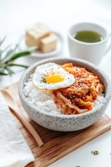 Rustic stone bowl with rice, kimchi, egg, and tea in warm light