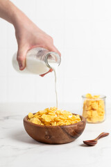 milk from a bottle pouring into a bowl with cornflakes, light background, breakfast