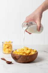 milk from a bottle pouring into a bowl with cornflakes, light background, breakfast