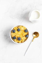 cornflakes with blueberries in a bowl and milk on a light background, breakfast