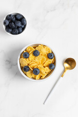 cornflakes with blueberries in a bowl and milk on a light background, breakfast