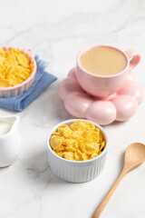 cornflakes in a bowl, milk and a cup of coffee on a light background, breakfast