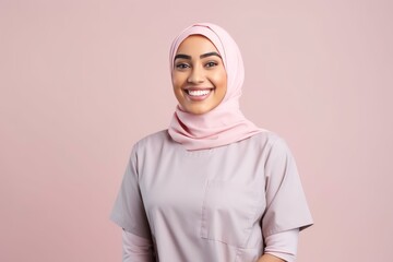 Portrait of smiling muslim doctor or nurse wearing pink hijab on pink background