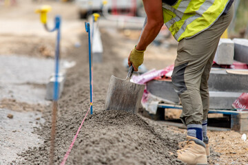 Worker expertly laying concrete for kerb line base on a construction site in bright safety gear 