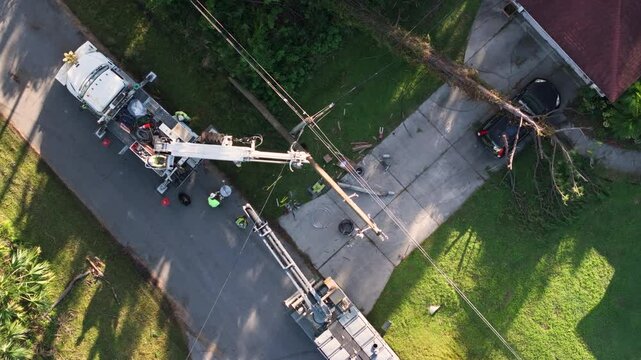 Hurricane aftermath in Florida. Workers using bucket trucks to repair blown down electrical wires at residential house. Utility services fixing damaged power lines.