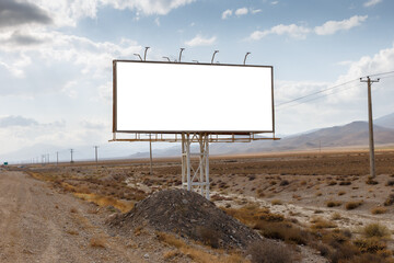 A blank billboard is positioned along a deserted road in a vast, open landscape under a cloudy sky.