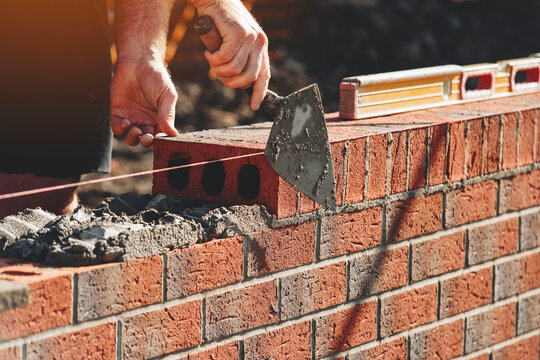 Bricklayer laying bricks to string line for a wall at a building site 