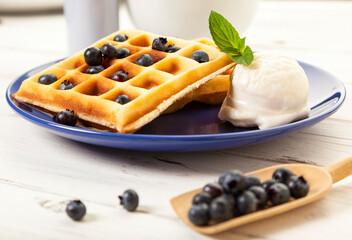 Belgian waffles with blueberries and vanilla ice cream scoop on blue plate, on rustic wooden table, shallow depth of field