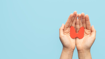 World Thyroid Day concept. Human hand holding thyroid gland shape made from paper on blue background. Awareness of thyroid disease such as hyperthyroidism, hypothyroidism and thyroiditis.