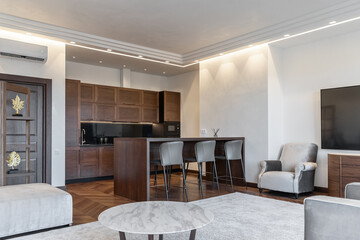 modern living room and kitchen design with matching furniture theme set. large TV, grey armchairs, wooden kitchen table and chairs. Wooden kitchen. Grey carpet, white walls, ceiling. Elegant interiors