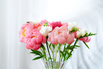 Vibrant peonies and delicate flowers in a glass vase create a serene atmosphere in a softly lit room