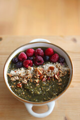 Beige bowl with green smoothie, frozen berries and homemade granola, served on the table. Selective focus.