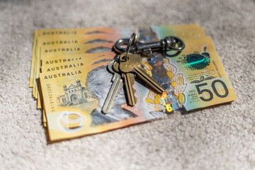 Close-up of a set of house keys resting on top of a bundle of fifty Australian dollar notes, with shallow depth of field. Concept: real estate, rental property, accommodation. 