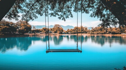 Serene lakeside swing under tree canopy.